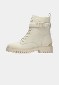 Beige Kampfstiefel mit geprägtem Blumenmuster, Schnürverschluss vorne, knöchelhoch, goldfarbene Metallteile und eine robuste, profilierte Sohle.