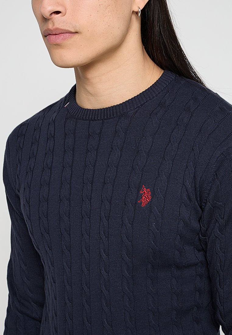 Marineblauer Cable-Knit-Pullover aus Textilstoff, mit einem gerippten Ausschnitt und kleinem roten gestickten Logo auf der Brust.