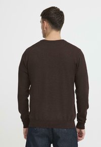 Brun strikkegenser laget av mykt stoff, med rund hals, lange ermer og ribbestrikket kant, med en teksturert overflate.