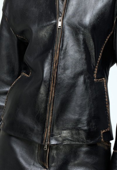 Black leather jacket with a front zipper, featuring a smooth texture, stitched accents, and a structured design.