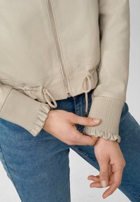 Helle beige Lederjacke mit einem Reißverschluss, gerafftem Bund und gerippten Bündchen. Strukturiertes Finish und verstellbare Kordeln am Bund.