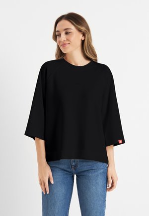 Zwarte oversize sweatshirt met een ronde halslijn en een gevalde schouderontwerp. Voorzien van een klein logo in het midden en een rode accent op de mouw.