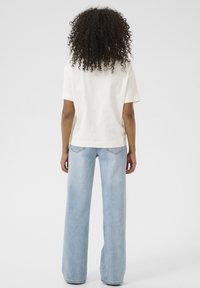 T-shirt en coton blanc à manches courtes et à coupe droite, associé à un jean large bleu clair avec poches arrière et coutures discrètes.