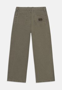 Grønne vide bukser laget av bomull, med to baklommer og et vevd merkelapp. Stoffet har en myk, teksturert overflate.
