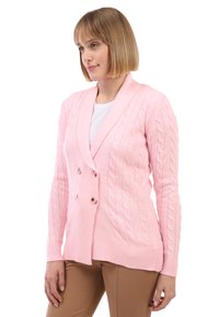 Cardigan rosa a maglia con design a doppio petto, caratterizzato da una texture a treccia e polsini a coste, abbinato a una maglietta bianca e pantaloni beige.