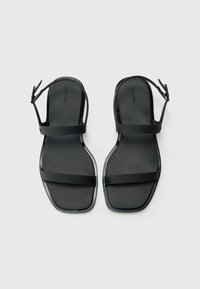 Black flat sandals made of rubber, featuring two wide straps and an adjustable ankle strap. Smooth surface with a square toe design.