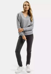 Jasnoszary sweter w serek z ribbowymi mankietami i dolnym wykończeniem, zestawiony z ciemnymi rurkami i białymi trampkami. Gładka tekstura materiału.