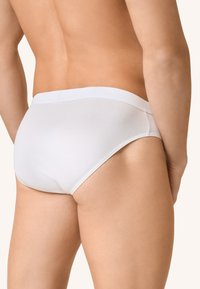 Mutande bianche da uomo in cotone con una superficie liscia e una vita elasticizzata, che mostrano una vestibilità contenitiva e un design minimalista.