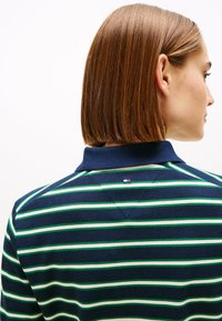 Polo bleu marine avec des rayures horizontales vertes et blanches, doté d'un col et d'un petit logo à l'arrière près de l'encolure.