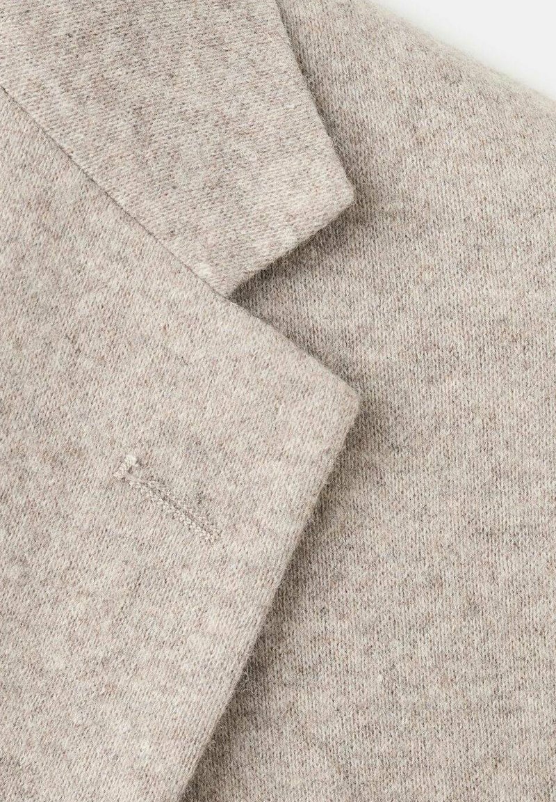 Hellbeiger Wollblazer mit strukturierter Oberfläche, Revers mit Kerbkragen und einer Brusttasche. Sauber geschnittene, maßgeschneiderte Kanten betonen das Design.