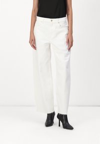 Pantaloni in denim bianchi a gamba larga con orlo sfrangiato, caratterizzati da vita alta e passanti per cintura, abbinati a stivaletti neri con tacco.