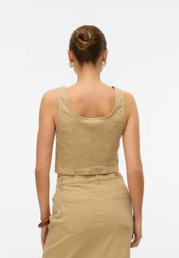 Beige crop-top med brede stropper, rund halsudskæring og stikninger, parret med en højtaljet beige nederdel med to baglommer.