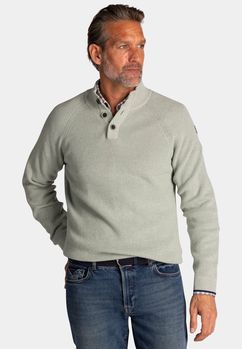 Lichtgroene geribbelde trui met een hoge kraag, knoopaccenten en lange mouwen. Gecombineerd met blauwe spijkerbroek en een geruite shirt eronder.