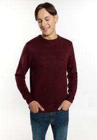 Maglione girocollo bordeaux realizzato in tessuto a maglia testurizzato, con maniche lunghe e polsini a coste, abbinato a jeans blu.