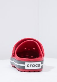 Crvene gumene Crocs cipele s izrezbarenim dizajnom, s crno-bijelim prugastim potplatom, zaobljenim stražnjim dijelom i udobnim pristajanjem.