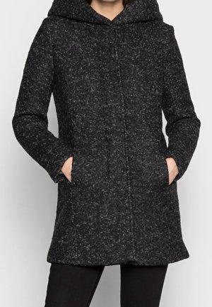 Cappotto nero texturizzato con cappuccio, dotato di una linea dritta, due tasche laterali e un motivo a pois sottile su tutto il tessuto.