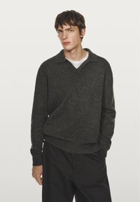 Donkergrijze pullover met een kraag, gemaakt van textuur gebreid stof. Draag het over een wit shirt, gecombineerd met zwarte broek.