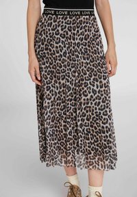 Midi-hame, jossa on leopardikuvio ja pleat, mustalla elastisella vyötärönauhalla, jossa on toistuva "LOVE"-teksti, käytetty vaaleanbeigejen sukkien ja ruskeiden nauhakenkien kanssa.