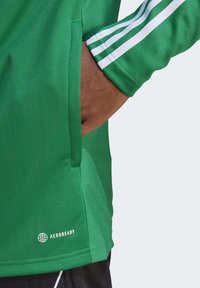 Groen sportshirt van een textuurstof, met witte strepen op de mouwen en een Aeroready-logo dichtbij de zoom.