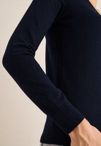 Maglione lavorato a maglia blu navy con scollo a V e maniche lunghe, con polsini e cuciture laterali a coste, realizzato in tessuto morbido.