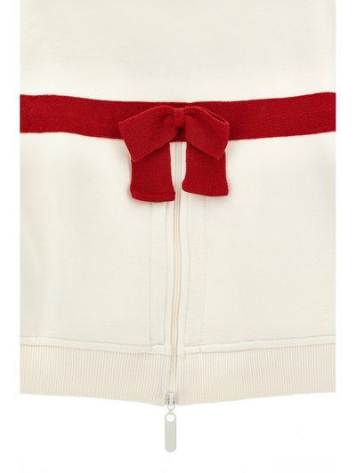 Section de vêtement blanche avec fermeture éclair verticale et nœud rouge tricoté horizontal noué au-dessus de la fermeture éclair.