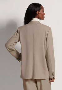Beige blazer met een smalle pasvorm, een gladde textuur, lange mouwen en een enkele achtervouw. Met knopen aan de mouwen en zonder zichtbare patronen of accenten.