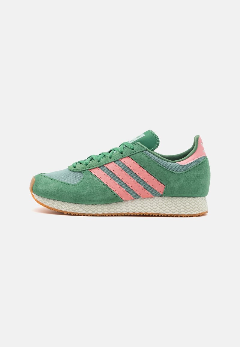 Green and pink suede sneaker with three pink stripes, a textured white midsole, and a rubber outsole. Features a rounded toe and lace-up design.