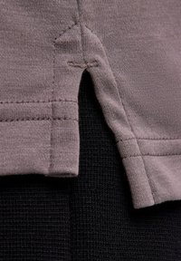 Jasnoszara tkanina o gładkiej fakturze z bocznym rozcięciem i widocznym przeszyciem. Odzież jest nałożona na fakturowany czarny materiał.