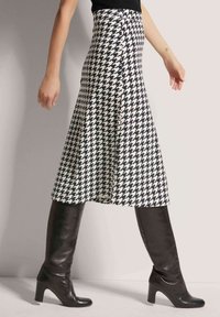 Schwarz-weißer Hahnentritt-Midi-Rock in fließendem Design, kombiniert mit kniehohen schwarzen Lederstiefeln, die eine schlanke Silhouette betonen.