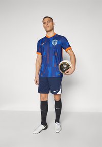 Nike blå fodboldtrøje med orange accenter, featuring et løvevåben, parret med marineblå shorts og sorte sokker. Bolden holdes foran.