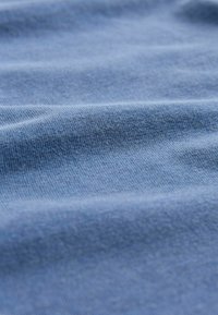 Tessuto di cotone azzurro chiaro con una texture liscia, caratterizzato da pieghe morbide e uniformi e sottili variazioni di colore.