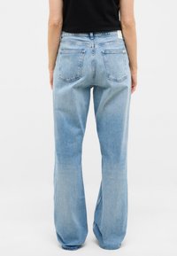 Jeans de mezclilla azul claro con un ajuste holgado, piernas rectas y dos bolsillos traseros. Presenta una pequeña etiqueta blanca en la cinturilla.