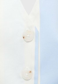 Bluza s gumbi iz mehkega bombažnega blaga z ozorcem v svetlo modri in bež barvi; vsebuje prozoren gumb blizu V-izreza.