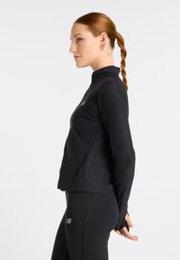 Black long-sleeve top with a high collar and thumbholes, made from a textured fabric, featuring a subtle logo on the chest.