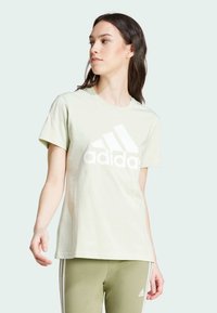 Camiseta de algodón verde claro con un gran logo blanco de Adidas en el frente, cuello redondo, mangas cortas y corte relajado.