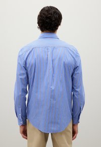 Camicetta a maniche lunghe da uomo in azzurro chiaro con righe verticali. Presenta un colletto classico, polsini con bottone e un fondo arrotondato, realizzata in tessuto morbido.