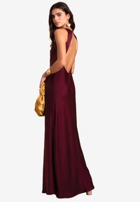 Abito da sera borgogna realizzato in raso morbido, con un design senza schienale, silhouette aderente e accessori dorati inclusi una pochette e un bracciale.