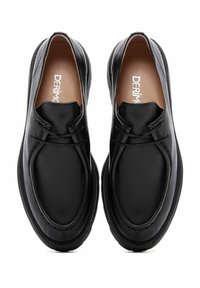 Zapatos de cuero negro con un diseño redondeado, sin cordones visibles y con una textura suave. Superficie lisa con detalles de costura sutiles.