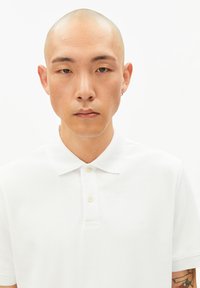 Wit poloshirt met een klassieke kraag, een drieknopensluiting en een subtiel logo op de borst. Soepele, ademende stoftextuur.