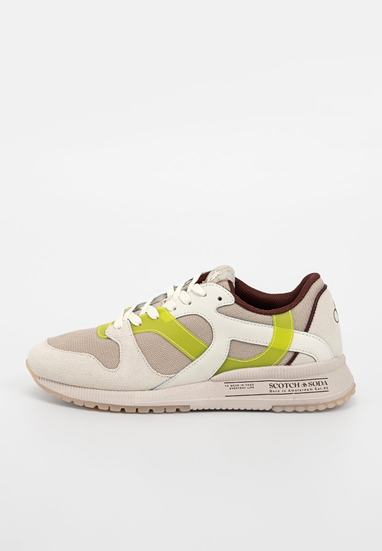 Botte de sport beige avec des accents verts et blancs, dessus en daim texturé et arrière brun. Présente une semelle légère et un logo bien visible.
