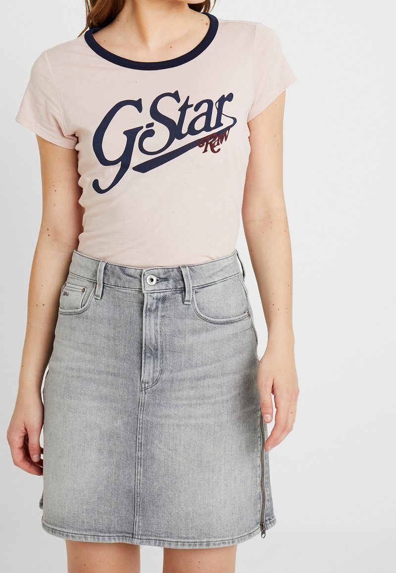 T-shirt rose clair avec encolure marine et grand logo "G-Star RAW" marine, associé à une jupe en denim grise ajustée avec une fermeture éclair sur le devant.