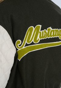 Mørk grøn jakke med en hvid quiltet læderærme, der har et forhøjet gul-grønt "Mustang" logo langs en hvid accentstribe.