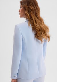 Jasnoniebieska marynarka o dopasowanym kroju, z klapami i guzikami na rękawach. Gładki materiał i czyste linie podkreślają fason.