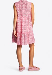 Vestido sin mangas rosa con un diseño en capas, que presenta una tela estampada y un dobladillo con volantitos. Combinado con sandalias rosas para un look completo.