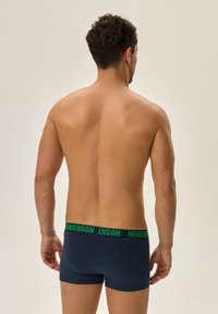 Granatowe bokserki wykonane z gładkiego materiału z zielonym elastycznym pasem z logo "HENDERSON". Model widoczny z tyłu.