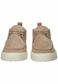 Zapatos de ante beige con punteras redondeadas, cordones y un diseño de caña alta. Incluyen una suela de goma blanca y una marca en la lengüeta.