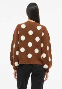 Suéter de punto marrón con grandes lunares blancos, con mangas abullonadas y dobladillo corto. Textura suave y ajuste relajado.