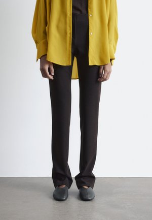 Yellow long-sleeve shirt in lightweight fabric, black slim-fit trousers, and gray slip-on shoes, all shown in a neutral setting.