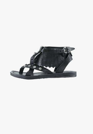 Sandale gladiateur en cuir noir avec franges à la cheville, clous argentés et bride réglable avec boucle sur semelle plate.