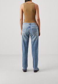 Ljusblå denimjeans med avslappnad passform, med bakfickor och en lätt blekning. I kombination med en brun ärmlös topp.